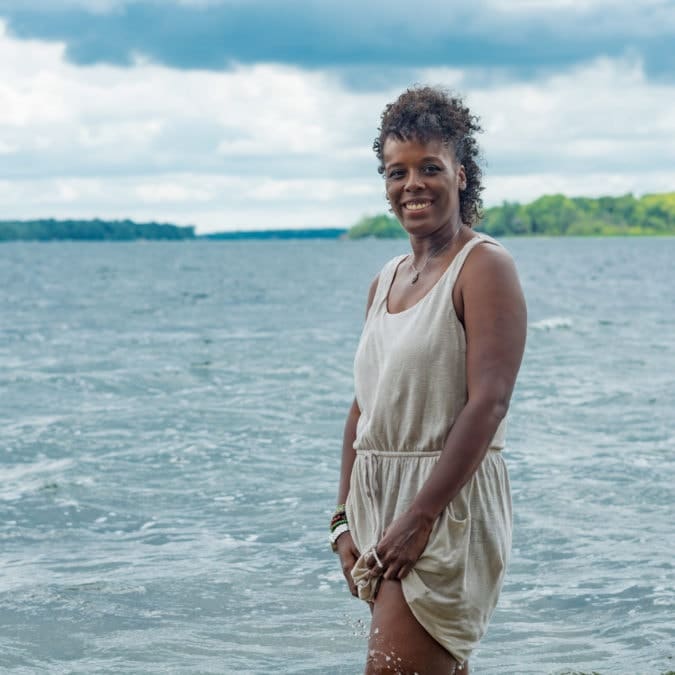 a woman stands and smiles by a lake