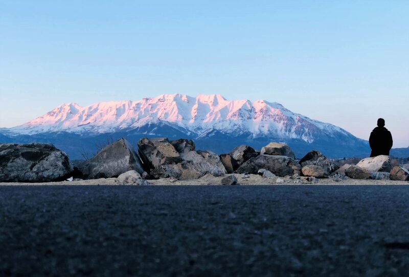Person sitting on rocks with snow-capped mountains in the distance